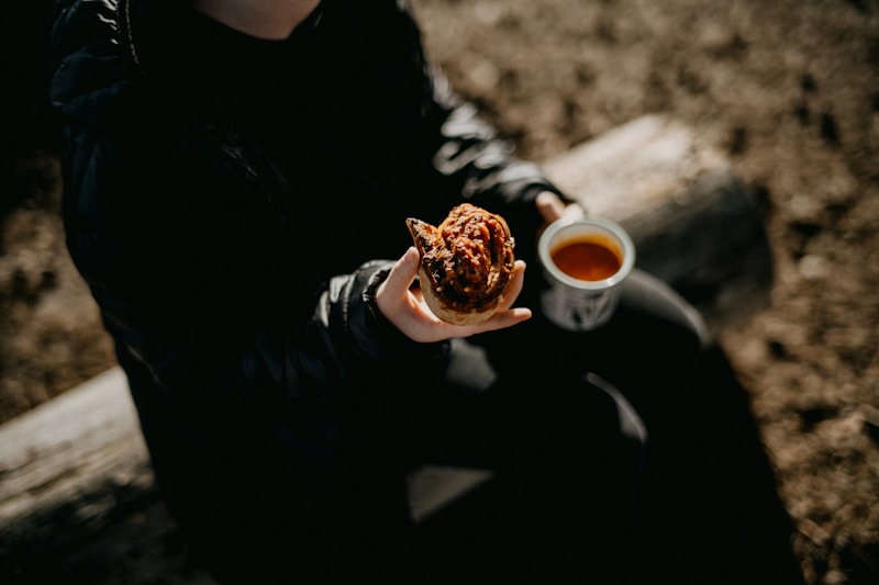 A person sitting on a bench holding a doughnut and a cup of tea