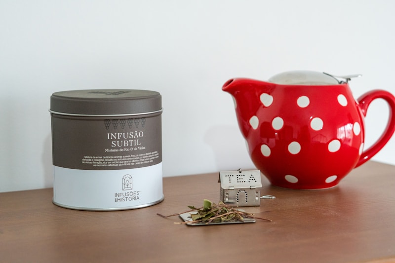 A red polka dot tea pot next to a tin of tea
