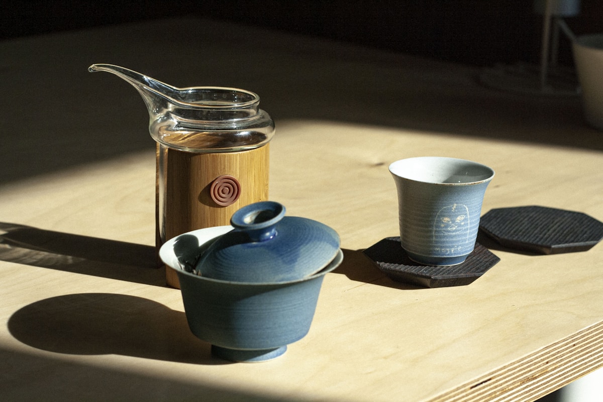 Blue ceramic teapot beside white ceramic mug on brown wooden table